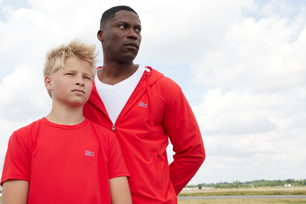 Mann mit roter Trainingsjacke mit Kapuze und weißem Shirt und Jacke und Junge mit rotem T-Shirt