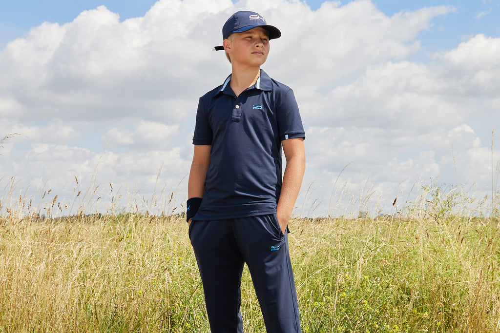 Junge in dunkelblauer Sportkleidung von Sportkind bestehend aus Polo Shirt, langer Hose, Sun Visor und Schweißband